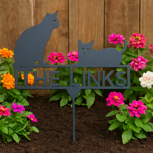 Metal sign with cat designs and 'THE LINKS' text in a garden setting with flowers.