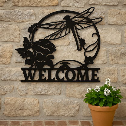 Decorative metal 'WELCOME' sign with a dragonfly design on a stone wall, accompanied by a potted plant.